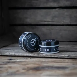 Judith & Gösta zinkpasta i svarta burkar med logotyp, naturlig skyddande zinksalva för häst mot hudirritation och skav, fotograferad på rustikt träunderlag