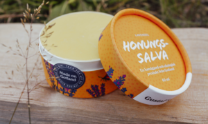 Lavendel honungssalva från Gustaf och Linnea i pappförpackning med naturligt bivax och honung placerad på trä i utomhusmiljö för ekologisk hudvård